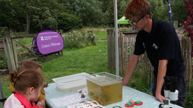 A member of Erddig Grow helps two young visitors identify what pondlife can be found in the Mindful Garden at Felin Puleston, Erddig